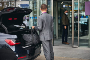 Driver in an elegant suit looking at his passenger standing at the airport terminal entrance