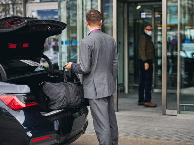 Driver in an elegant suit looking at his passenger standing at the airport terminal entrance at san diego international airport on the way to LAX