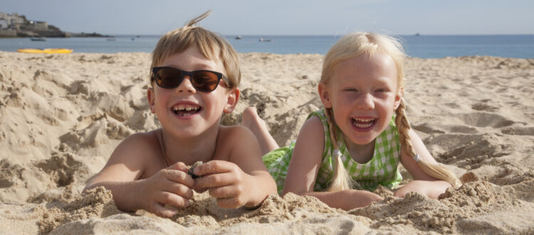 A boy and girl lying at Mission Beach, San Diego, on their stomachs on the sand, laughing and looking at the camera.